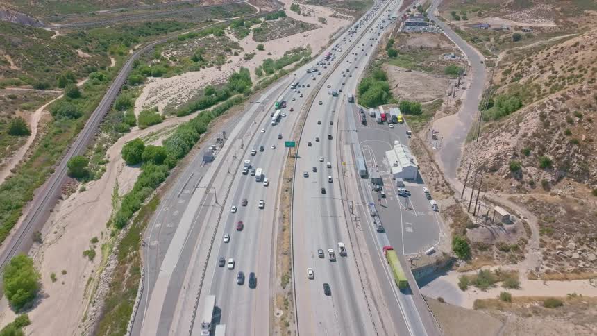 Aerial footage captures a busy multi-lane highway and a parallel freight train carving through a vast, arid mountain valley