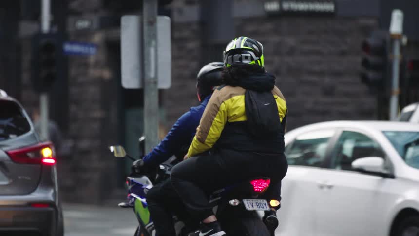 A slow-motion view from behind of two people on a motorcycle waiting in city traffic