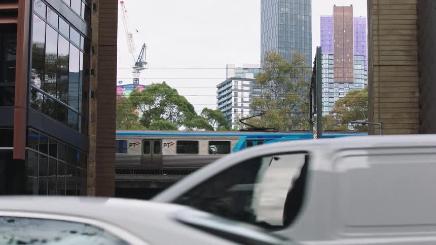 A slow-motion view of a commuter train traveling over a bridge in a modern city as cars drive by below