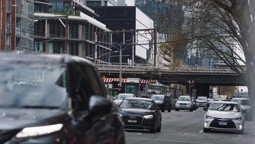 A slow-motion, eye-level shot of city traffic moving under a railway overpass with modern buildings in the background