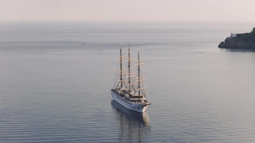 A majestic tall ship is anchored in the calm waters of the Mediterranean Sea near a verdant coastline