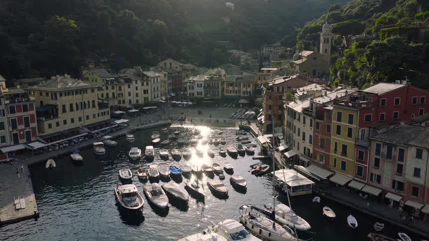 Golden sunlight reflects on the tranquil water of the picturesque Portofino harbor, filled with boats and surrounded by colorful Italian buildings