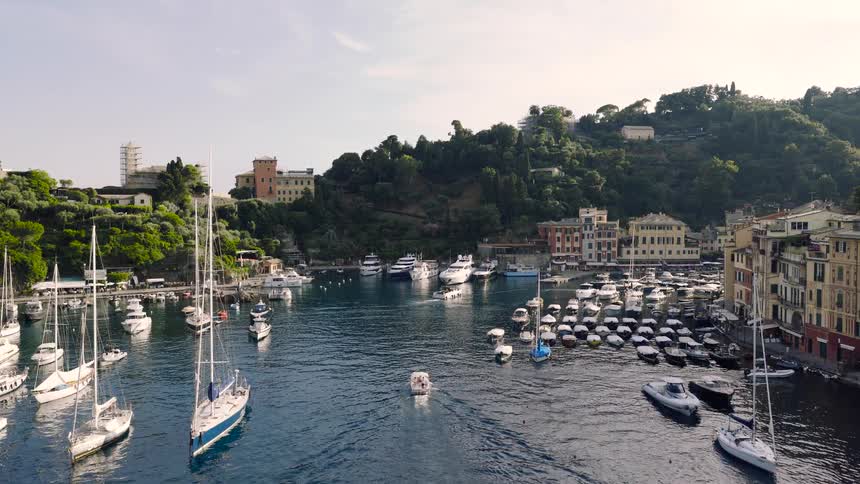 Aerial view of the picturesque harbor of Portofino, Italy, filled with luxury yachts and traditional boats nestled against a lush green hillside