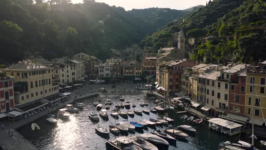 An idyllic aerial shot slowly pushes towards the charming Portofino harbor in Italy, showcasing colorful buildings and numerous boats during a golden sunset