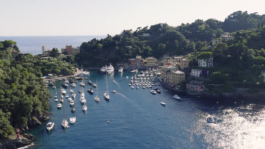 A slow aerial pullback reveals the stunning harbor of Portofino, Italy, filled with luxury yachts and sailboats on a sunny summer day