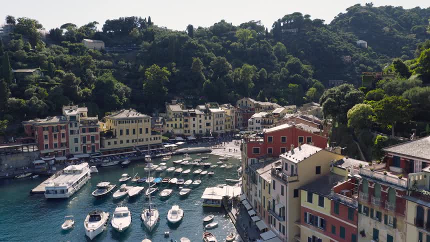 A scenic high-angle time-lapse of the iconic Portofino harbor in Italy, showcasing colorful buildings, a bay filled with boats, and people enjoying a sunny day
