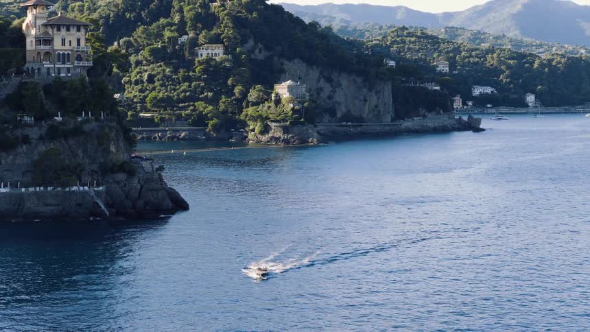 A luxury motorboat sails along the stunning Portofino coastline, with lush green mountains and elegant villas in the background