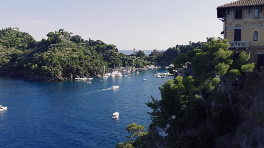 Stunning aerial footage slowly flies past a cliffside villa towards the beautiful and iconic harbor of Portofino, Italy