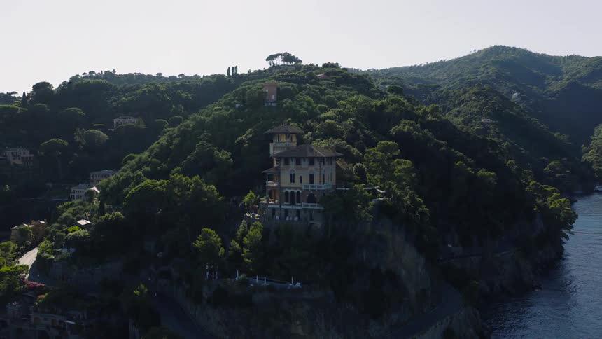 Aerial time-lapse of the sun rising over a beautiful coastal villa nestled in the lush green hills of Portofino, Italy