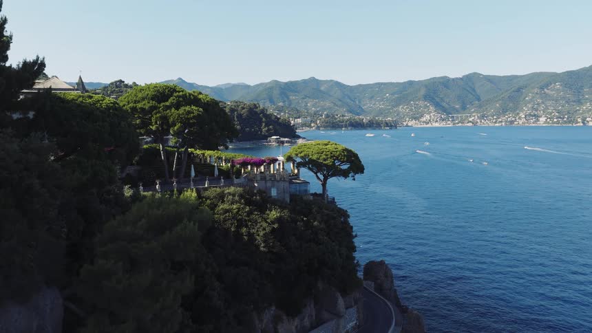 An aerial view of the beautiful Italian Riviera coastline, flying along a winding road to a luxurious villa perched on a cliff above the sea