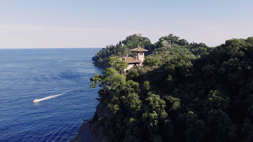 An aerial drone shot flies along the lush, green coastline of Portofino, Italy, revealing beautiful villas and a harbor full of yachts