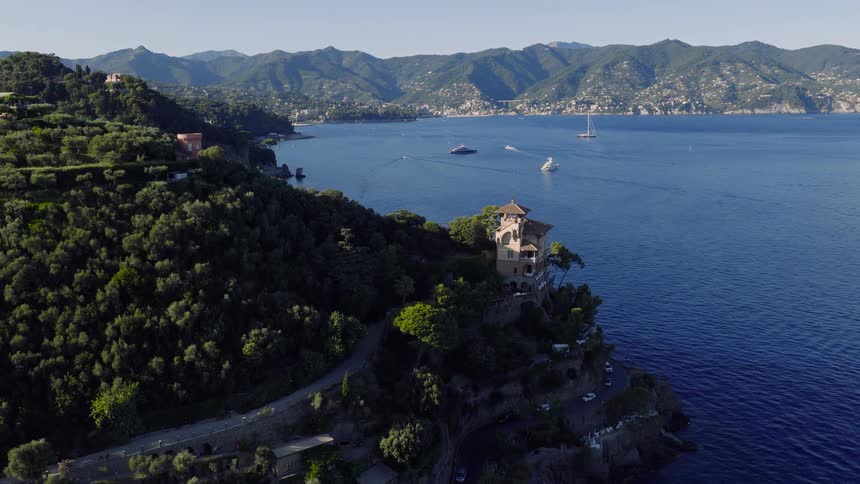 Stunning aerial view of the Portofino coastline with luxury villas perched on lush green cliffs overlooking the deep blue sea and distant mountains
