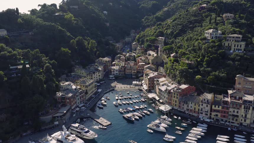 A stunning high-angle aerial view slowly pulls back to reveal the iconic harbor of Portofino, Italy, filled with luxury yachts and surrounded by colorful buildings