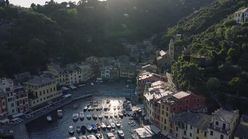 Stunning aerial view flying towards the picturesque harbor town of Portofino, Italy, as the sun sets over the green hills