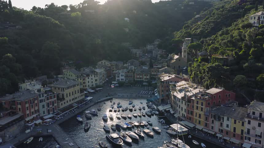 A stunning aerial view captures the sunlit harbor of Portofino, Italy, showcasing the iconic colorful buildings and numerous boats dotting the tranquil water