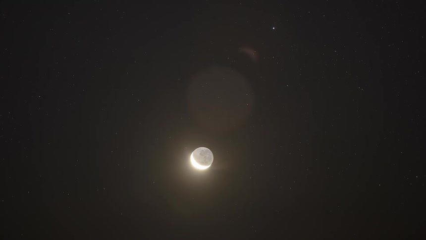 A timelapse of a crescent moon setting behind a mountain range under a starry night sky