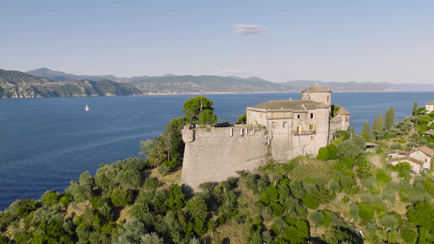 A beautiful static shot of a historic castle built on a lush green cliffside overlooking the serene blue sea on a sunny day