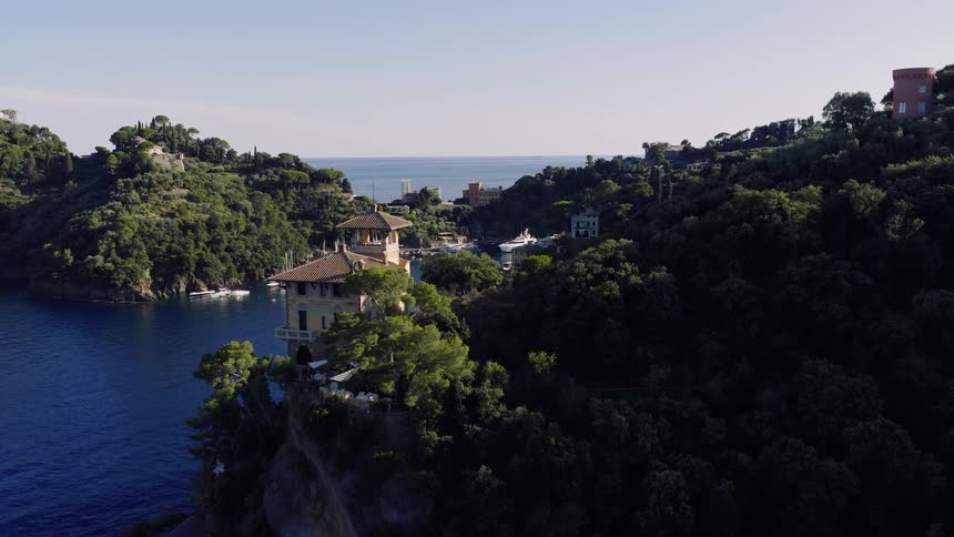 An aerial view slowly reveals the picturesque harbor of Portofino, Italy, nestled in a cove with yachts and villas along the lush green coastline