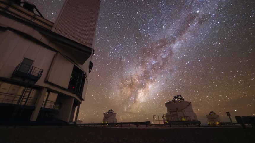 A stunning timelapse from a low angle shows the Milky Way galaxy moving across the starry night sky above large, rotating astronomical observatories