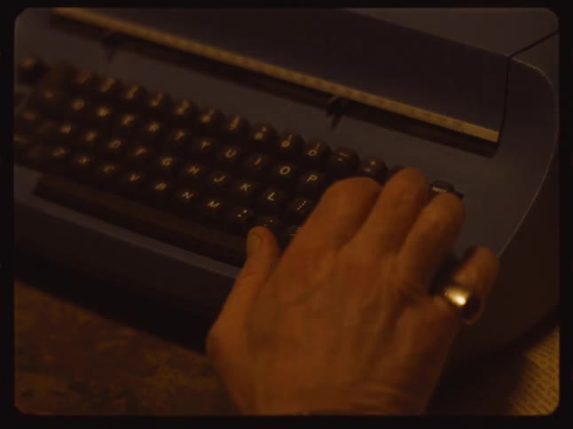 A writer's hand with a gold ring types on a vintage blue typewriter in this Super 8 style film clip