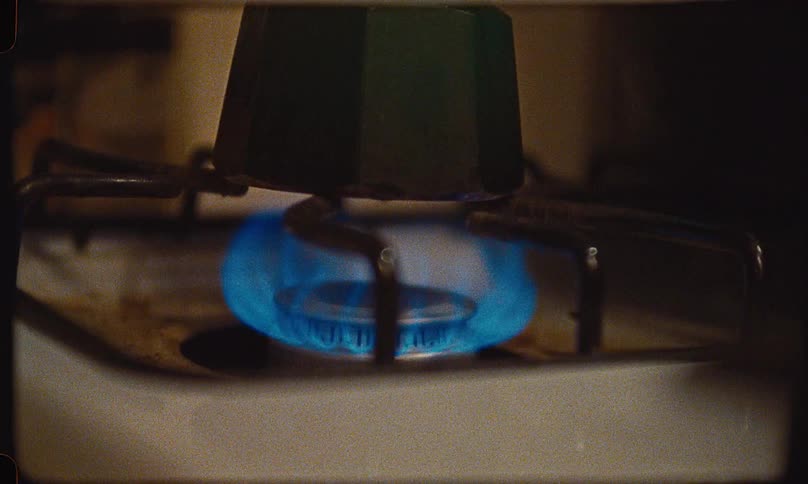Close-up of a vintage gas stove igniting to heat a green Moka pot coffee maker, shot on Super 8 film