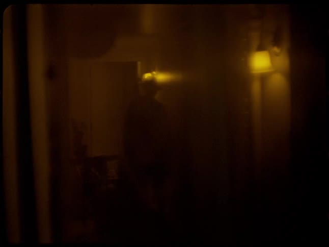 A haunting silhouette of a person stands in a dark, hazy room in a grainy, vintage film clip with prominent light leaks