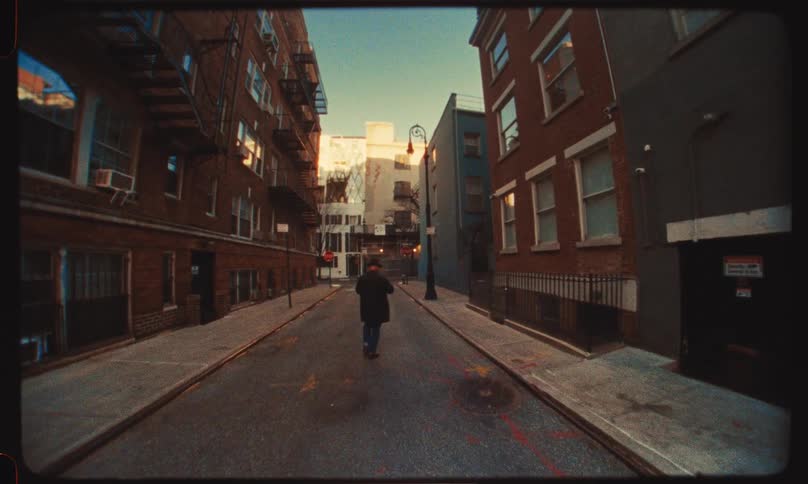 Retro-style footage follows a solitary man as he walks down an empty urban alley during golden hour