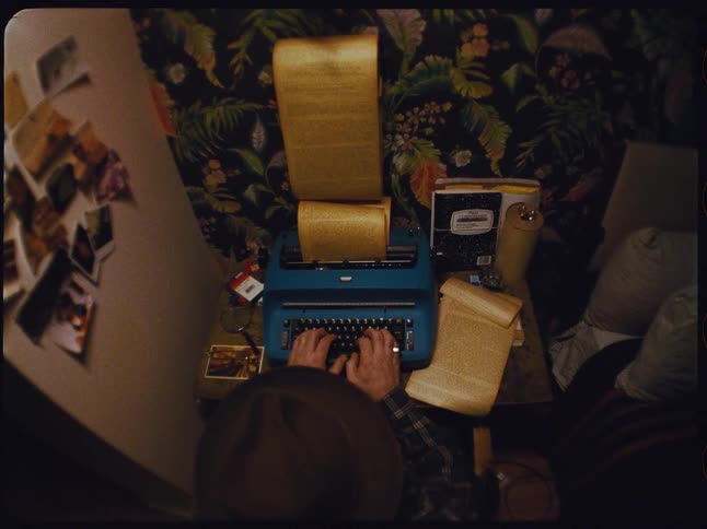High angle view of a writer endlessly typing a manuscript on a vintage blue typewriter in a dimly lit, retro-styled room