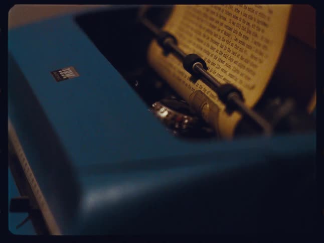 A moody, vintage film-style close-up shows a blue IBM electric typewriter with a page of text loaded in