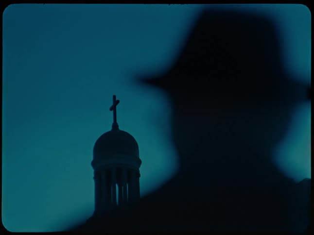 Mysterious Super 8mm footage shows the dark silhouette of a man in a hat observing a church steeple at night