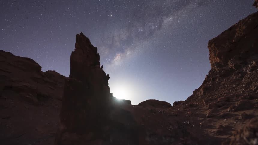 A breathtaking timelapse captures the Milky Way moving across the night sky, followed by a brilliant moonrise that illuminates the rocky desert canyon below