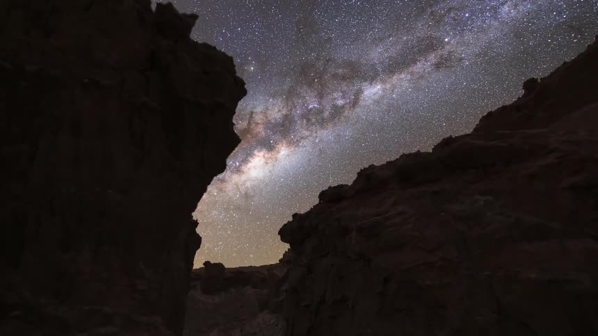 A stunning astrophotography timelapse of the Milky Way galaxy moving across the night sky framed between the silhouette of desert rock formations
