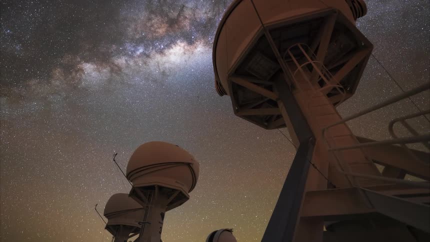 A low-angle time-lapse captures the magnificent Milky Way galaxy as it moves across the starry night sky above powerful astronomical observatory telescopes