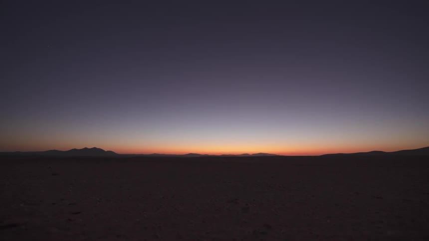 A breathtaking timelapse captures the transition from a vibrant sunset to a star-filled night sky over a vast desert landscape