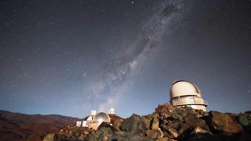 A stunning night sky timelapse reveals the vibrant Milky Way galaxy moving over astronomical observatories on a remote mountain