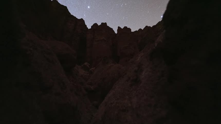 A day-to-night timelapse tilts up from within a narrow rock canyon to reveal the Milky Way and starry sky