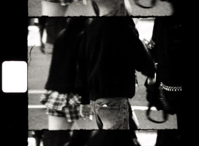 Black and white 8mm film captures the lower bodies of pedestrians walking over a Japanese 'Stop' sign on a city street