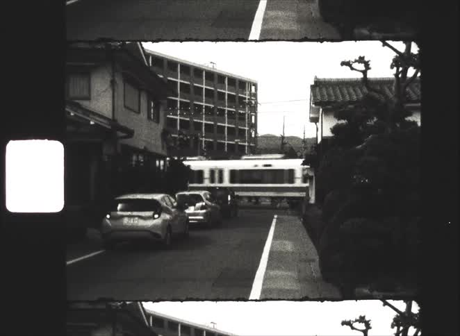 A train crosses a city street in Japan as cars wait in this vintage, black and white 8mm film footage