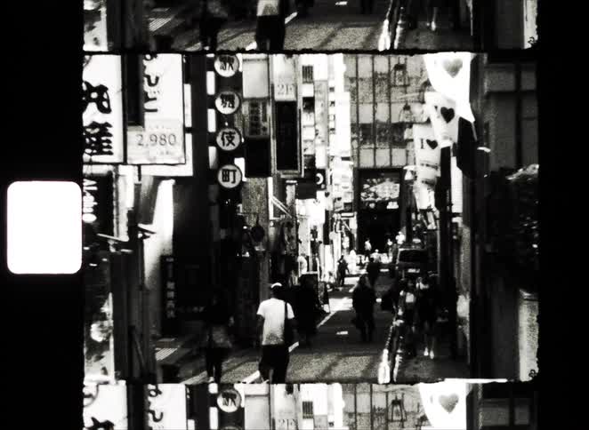 Abstract, grainy black and white film captures a time-lapse of pedestrians walking down a busy, narrow street in a Japanese city