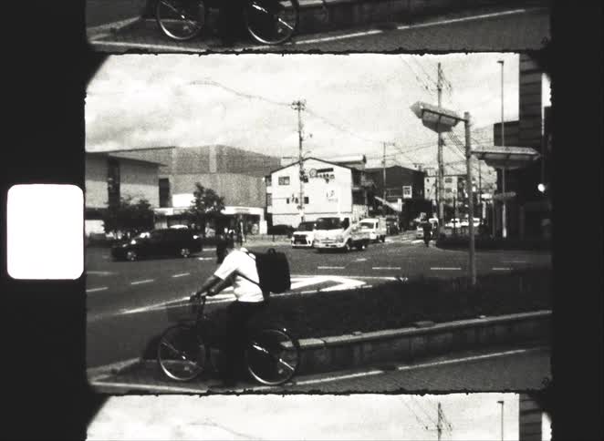 Vintage 8mm black and white footage shows a person on a bicycle waiting at a busy street corner in a Japanese city