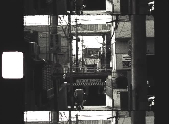 Vintage black and white film captures a person riding a bicycle down a narrow Japanese alleyway tangled with power lines