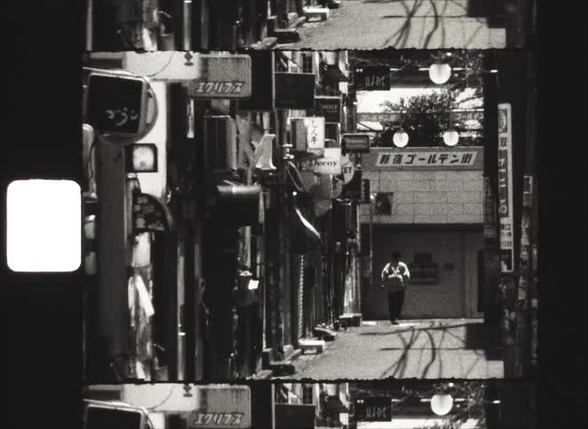 Vintage black and white 8mm film slowly zooms in on a lone person standing in a narrow, cluttered alley in Tokyo, Japan