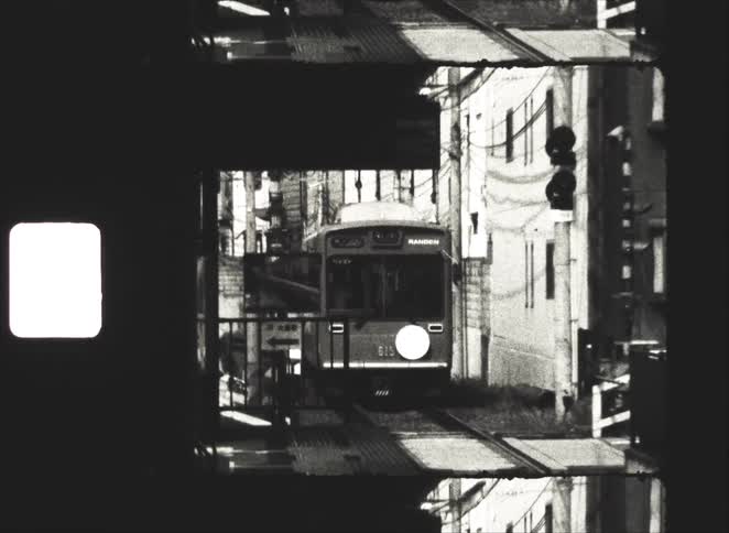 Vintage black and white 8mm film of a Japanese tram arriving at an urban train station