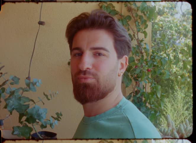 A handsome bearded man poses for a retro-style film portrait, giving a slight smile to the camera