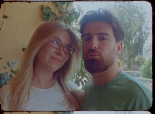 A vintage-style film portrait of a young couple looking at the camera on a sunny day