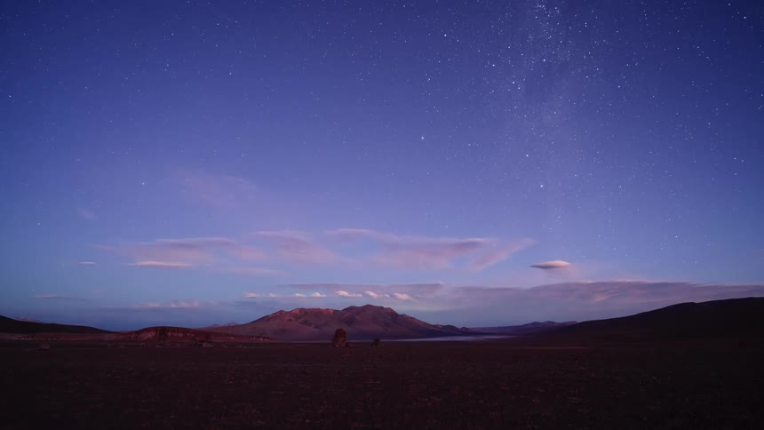 A breathtaking time-lapse captures the transition from a vibrant desert sunset to a spectacular starry night with the Milky Way rising over the mountains