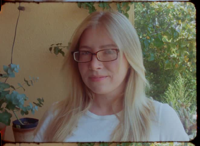 Vintage 35mm film style portrait of a smiling blonde woman with glasses as the wind blows her hair