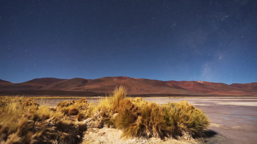 A night time-lapse reveals the Milky Way galaxy moving across the starry sky above the otherworldly landscape of a desert salt flat and mountains