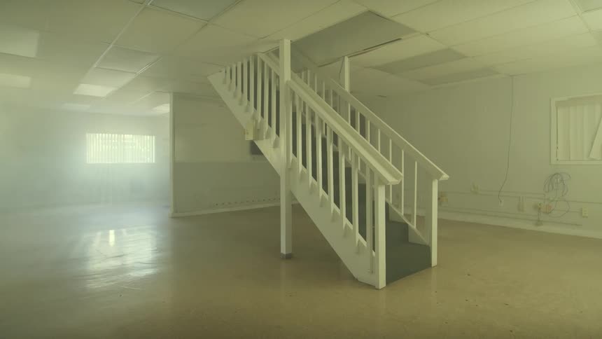 A mysterious, empty room filled with fog features a single staircase leading upwards as light streams through a window