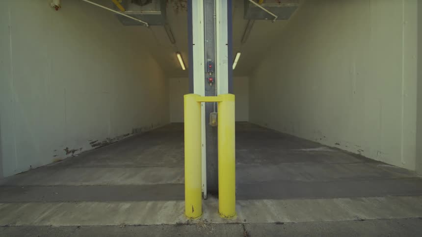 A slow camera tilt down from the sky reveals the entrance to a modern, empty industrial loading bay with twin roll-up doors